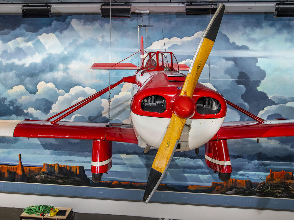 A red and white airplane hang in front of a mural of a Western landscape.