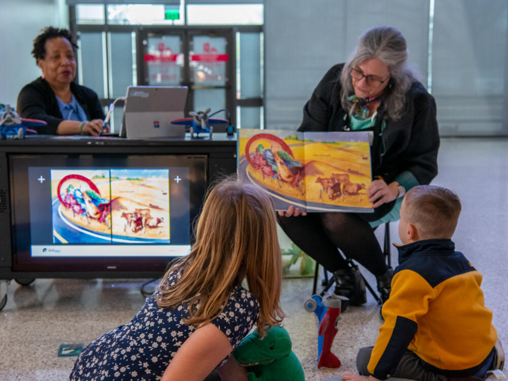 A museum educator reads a picture book to onlooking children. 